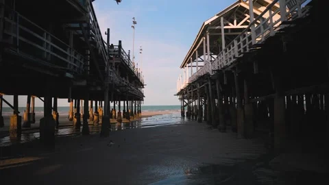 Wide view between two wooden piers on stilts, revealing wet sand and the distant Video stock 314765274
