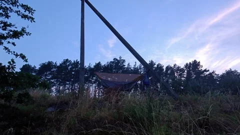 Wide view of camping hammock hanging between poles at evening dusk Stock Footage 339591922