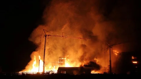 Wide view of construction site fire with cinders being lifted higher than cranes Stock Footage 93615720