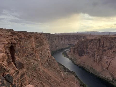 Wide view of deep canyon with winding river under dramatic sunset sky Foto stock