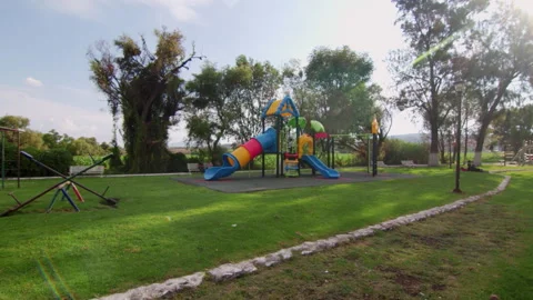 Wide view of an empty colorful playground in a sunny public park, with slides Stock Footage 340330573
