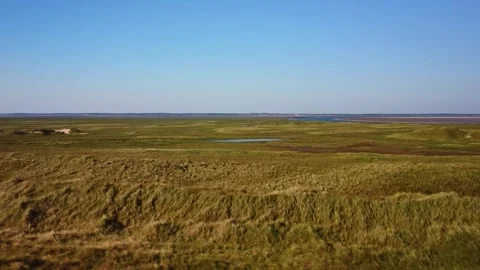 Wide view of grassy fields and water near a coastline taken during the day Stock Footage 339937175