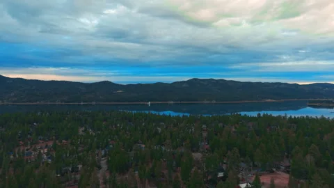 Wide view of Lake framed by forest and mountains under dramatic cloudy sky Stock Footage 328898751