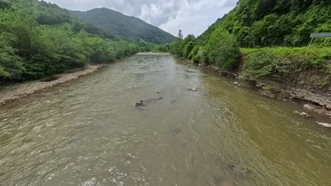 Wide view looking along a flowing mountain river flanked by steep forest slopes Vídeo Stock 346182133