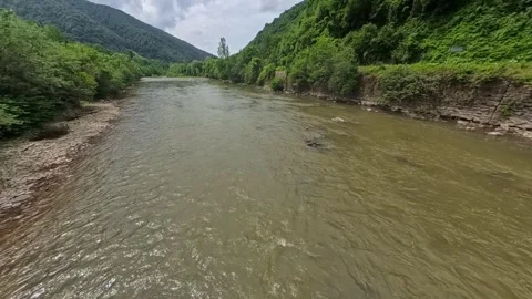 Wide view looking along a flowing mountain river flanked by steep forest slopes Vídeo Stock 346182135