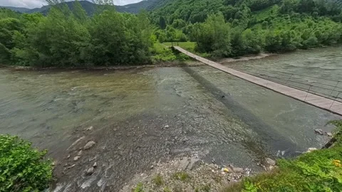 Wide view looking along a flowing mountain river flanked by steep forest slopes Vídeo Stock 346182170