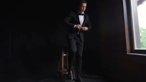 Wide view of man adjusts his suit and goes to the window. Dark room. Slow motion Stock Footage 242428080