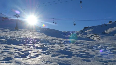 Wide view of moving empty ski lift and a man snowboarding from snowy mountain on Stock Footage 106475128