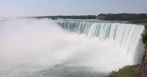 Wide view of Niagara Falls with mist, a lone bird, and tiny tourists below. Stock Footage 320024226