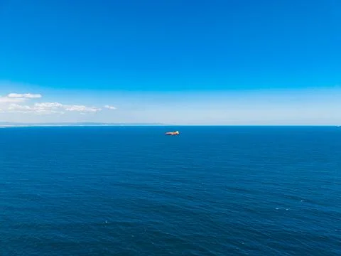 Wide view of the ocean with a distant ship on a clear day and a blue sky abov Stock-Fotos