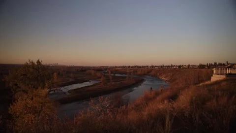 WIDE VIEW OF RIVER LANDSCAPE WITH DISTANT CITY SKYLINE AT GOLDEN HOUR Stock Footage 336950782