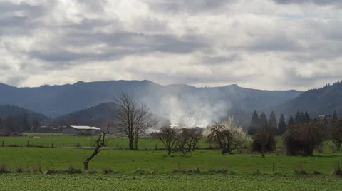 Wide view of rural fields with mountains in background; smoke rising from a Stock Footage 59534541