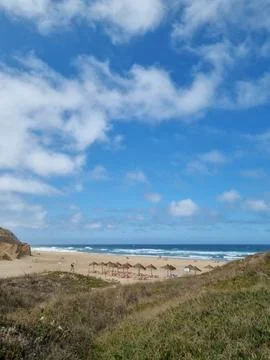 Wide view of a sandy Atlantic beach framed by coastal dunes and beach umbrell Фото