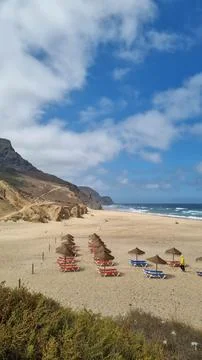 Wide view of a sandy Atlantic beach framed by coastal dunes and beach umbrell Фото