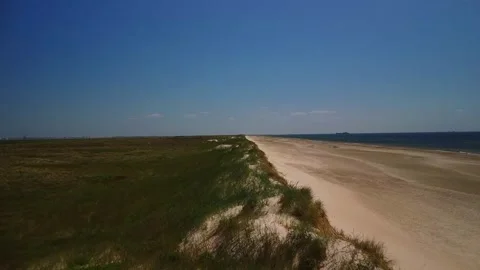 Wide view of sandy beach next to green grass and blue water on a sunny day .. Stock Footage 339938854