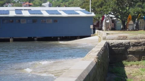 Wide view of a small boat ramp beside a waterfront sailing club building at Stock Footage 325973252