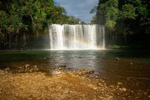 Wide View of Tad Champee Waterfall with Rainbow and Rocky Riverbed Stock Photos