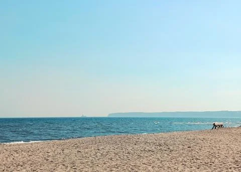 Wide view of a tranquil beach with sandy shore and calm blue sea under clea.. Foto stock