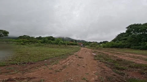 A wide view of Two Men Walk Along a Winding Dirt Road Through Green Fields Video stock 332352975
