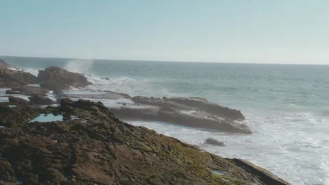 WIDE VIEW OF WAVES BREAKING AGAINST ROCKY COAST WITH SLOW UPWARD TILT Stock Footage 346515021