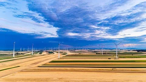 Wide view of wind turbines in a flat field under cloudy sky Stock Photos