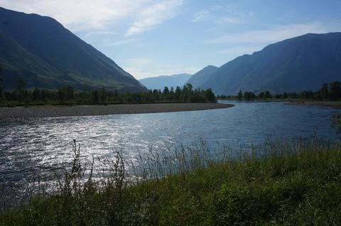 A wide winding river flows through a mountain valley on a clear summer day Stock Photos