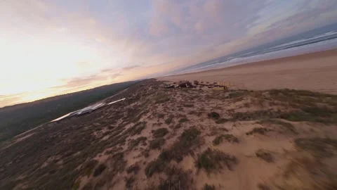 Widely open sandy beach at dawn, dune-covered land, parked cars, ocean horizon Stock Footage 344542754