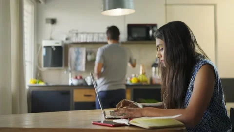 A wife is attending online classes while husband is working in the kitchen Stock Footage 151758146
