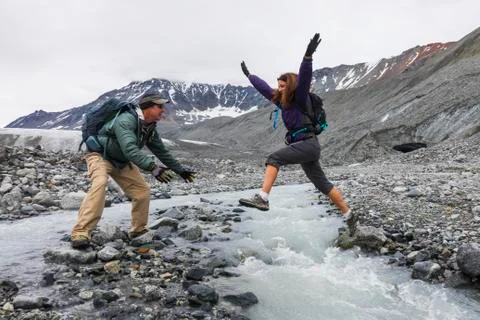 A wife jumps to her husband across an icy stream while hiking near Gulkana Glaci Stock Photos