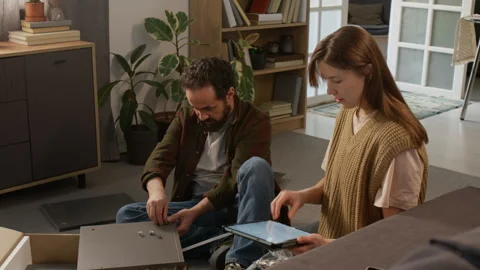 Wife with Tablet Assisting Husband Assembling Flatpack Cabinet at Home Stock Footage 330509841