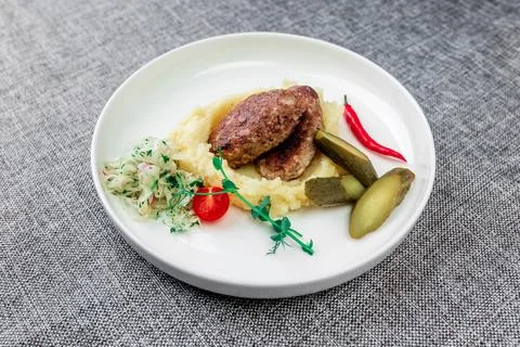 Wild boar cutlets with mashed potatoes. Served on a white plate with pickled Stock Photos