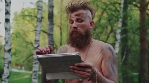 Wild Homo Sapiens Ancestor Using Modern Tablet PC or Mobile Computer in Forest Stock Footage 131291304