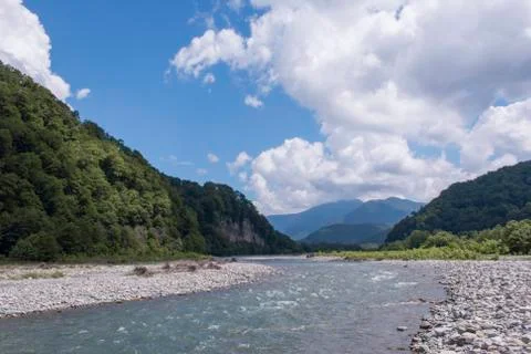 Wild river flowing between green mountains on a clear summer day Stock Photos