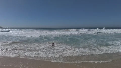 Wild surf with man standing in shallow water. Wide aerial view on sunny day Stock-Footage 347980027