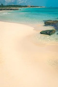Wild tropical sandy beach with clear turquoise waters, soft waves and rocks Stock Photos