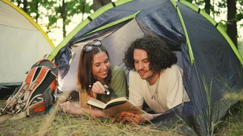 In the wilderness, a couple cuddles under a lantern, reading in their cozy tent Stock Footage 285369347