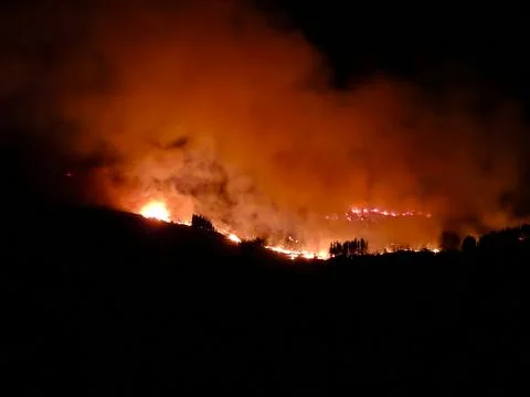 Wildfire burning mountainside creating intense orange smoke Stockfoto's