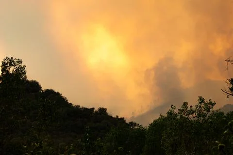 Wildfire burning mountainside, smoke creating atmospheric glow Stock Photos