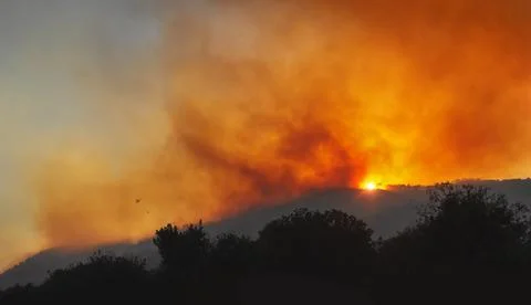 Wildfire on a mountain slope at sunset with dramatic red sky and heavy smoke Stock Photos