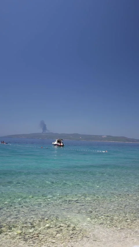 Wildfire smoke rises beyond calm turquoise sea Stock Footage 341319404