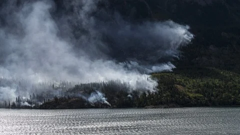 Wildfire smoking on side of mountain next to lake 8K time lapse Stock Footage 113990821