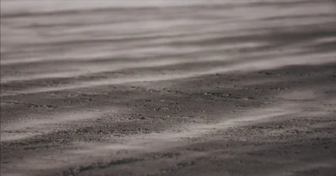 Wind blowing streaks of sand and dust over dark ground in slowmotion Stock Footage