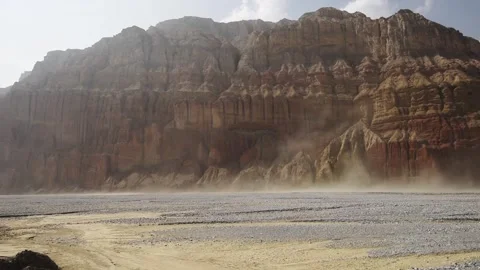 Wind-blown dust drifts past a red and ochre cliff wall in the Kali Gandaki Stock Footage 344530747