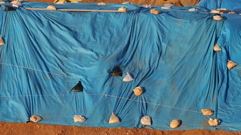 Wind blows blue tarp weighted down by sandbags protecting outdoor materials Stock Footage 231824924