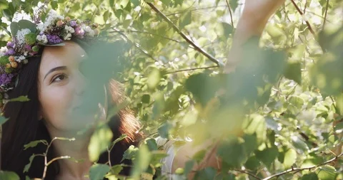 Wind blows leaves of green tree before face of a gorgeous woman dressed like a Stock Footage 95634670