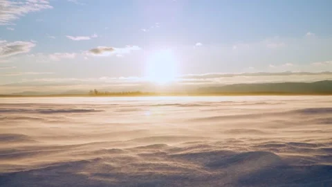 The wind blows snow off the snow-covered surface of the frozen lake at sunset. Stock Footage 266024575