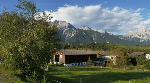 Wind blows trees in foreground with country farm in the Austrian Alps at sundown Stock Footage 50361313