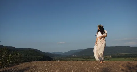 Wind blows woman's light white dress while she stands like a nymph before Stock Footage 95633569