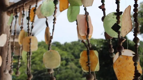Wind chimes swing in the wind on a windy afternoon with a green jungle backdrop. Vídeos de archivo 128114673
