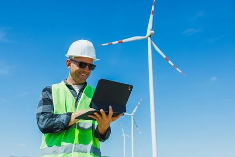 Wind energy worker checks data on a tablet while standing near wind turbine.. 스톡 사진